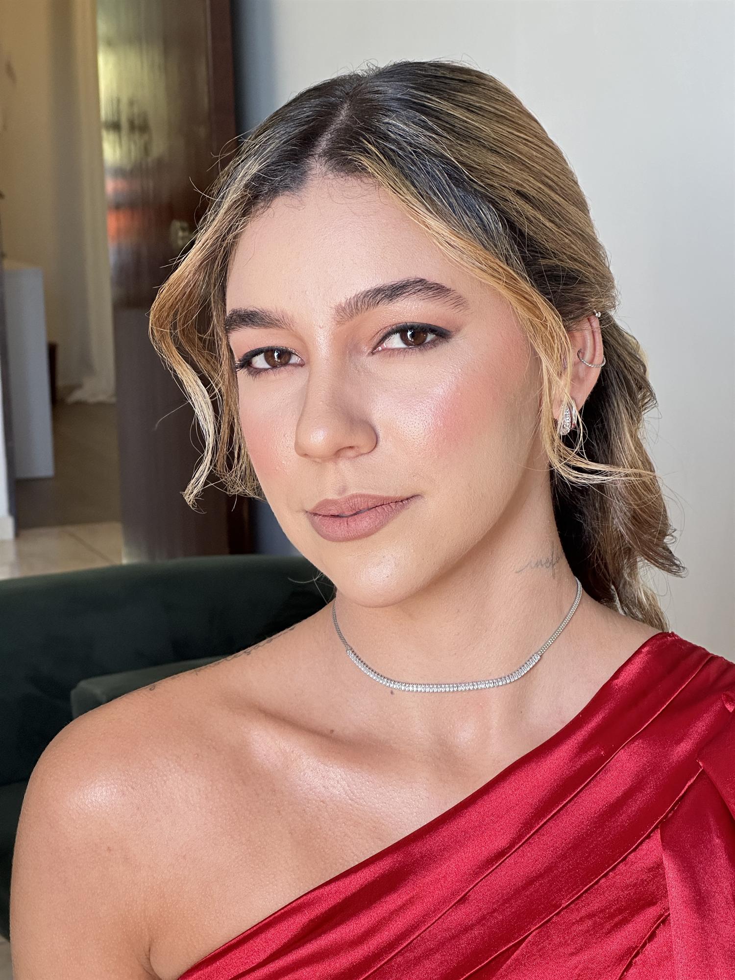 Convidada de vestido vermelho de um ombro só, com pele iluminada e ondas soltas
