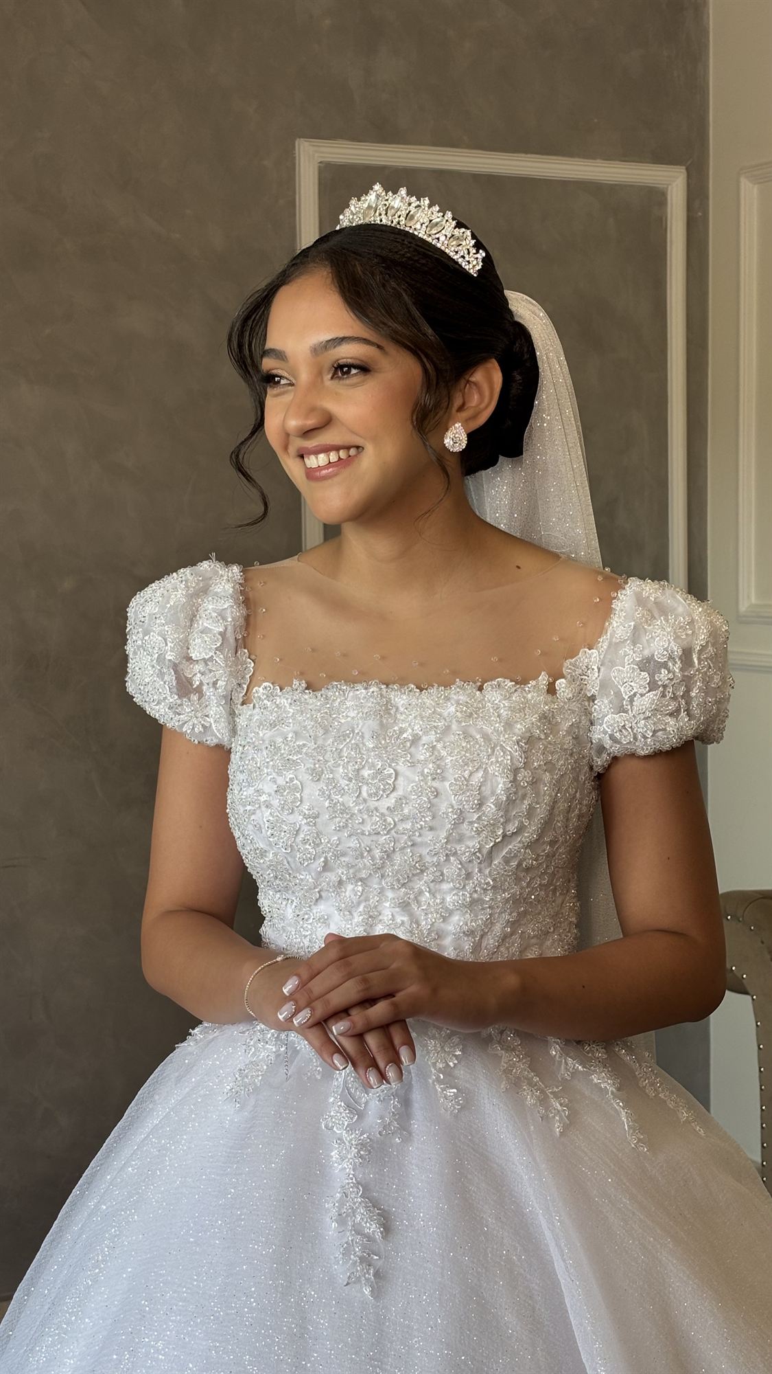 Noiva de tiara e vestido bordado sorrindo e olhando para o lado